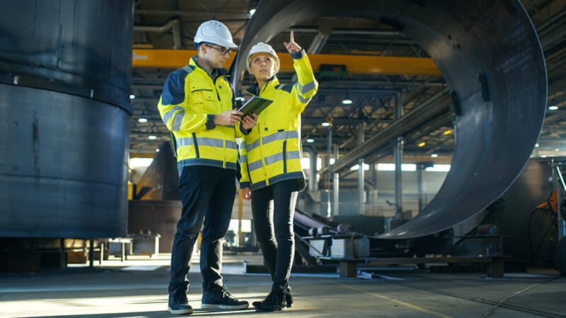 Zwei Personen stehen in Sicherheitskleidung in einer Fabrikhalle